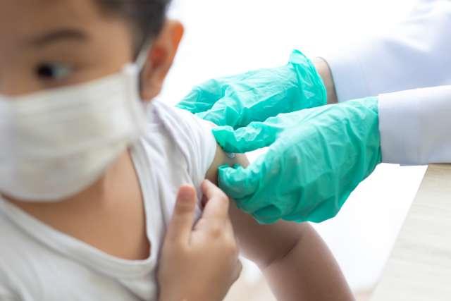 Pediatric doctor holds performing vaccination on child. 