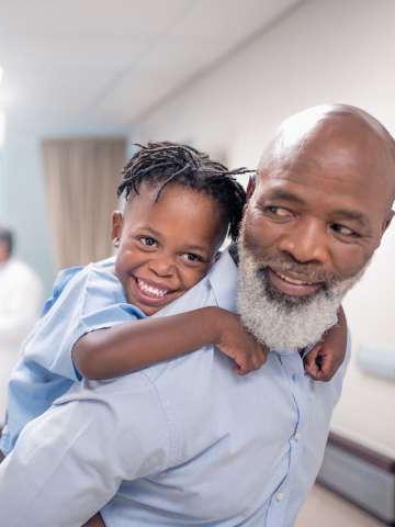 Bearded father giving piggyback to son at children's hospital.